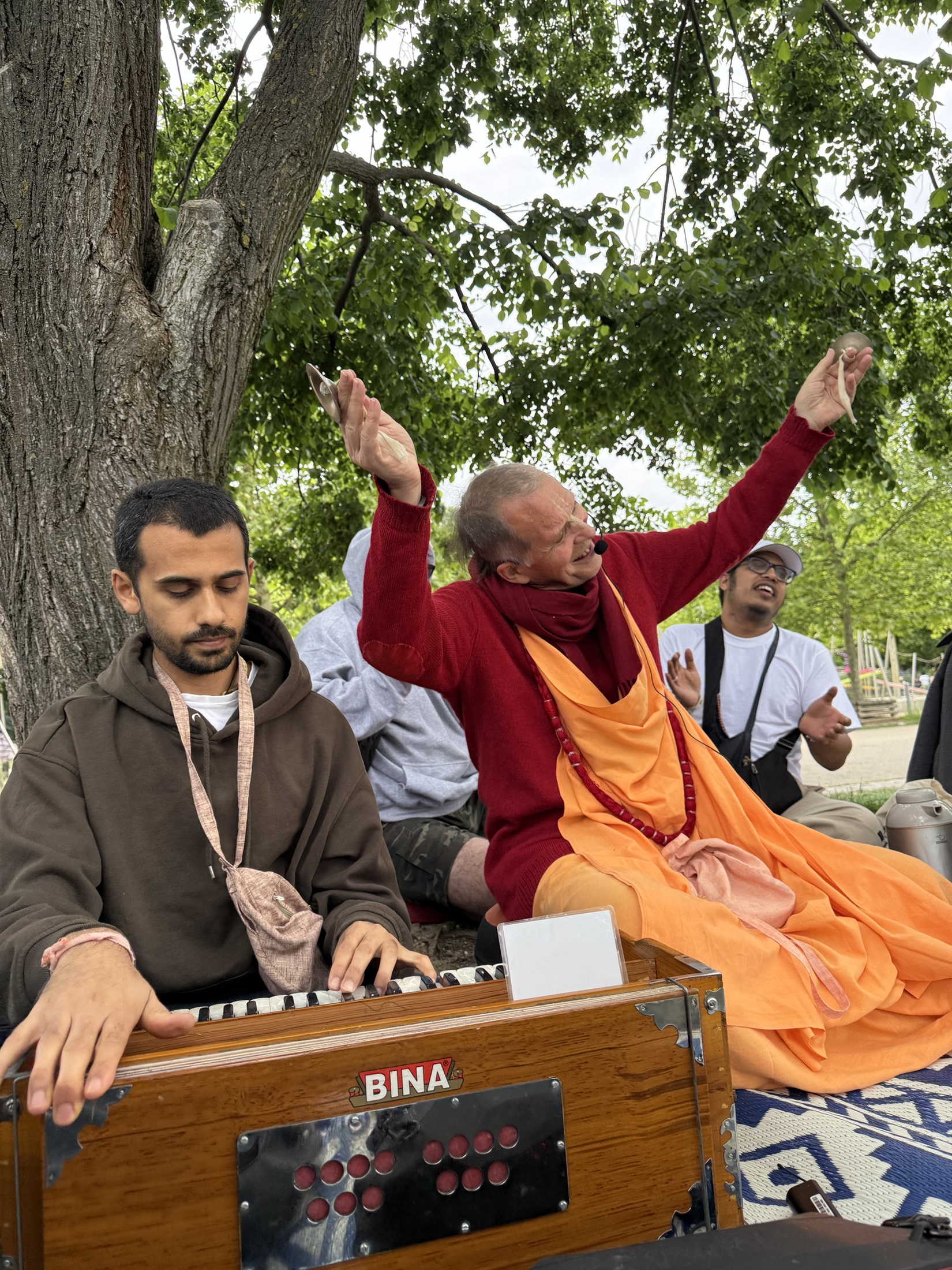 Kirtan-Musiker mit Harmonium unter einem großen Baum