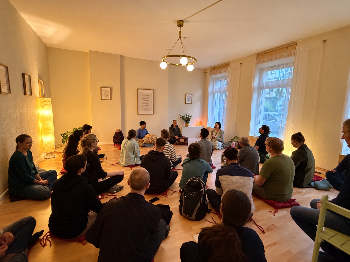 Menschen sitzen gemeinsam im Kreis bei einem Kirtan mit Harmonium und Mṛdaṅga